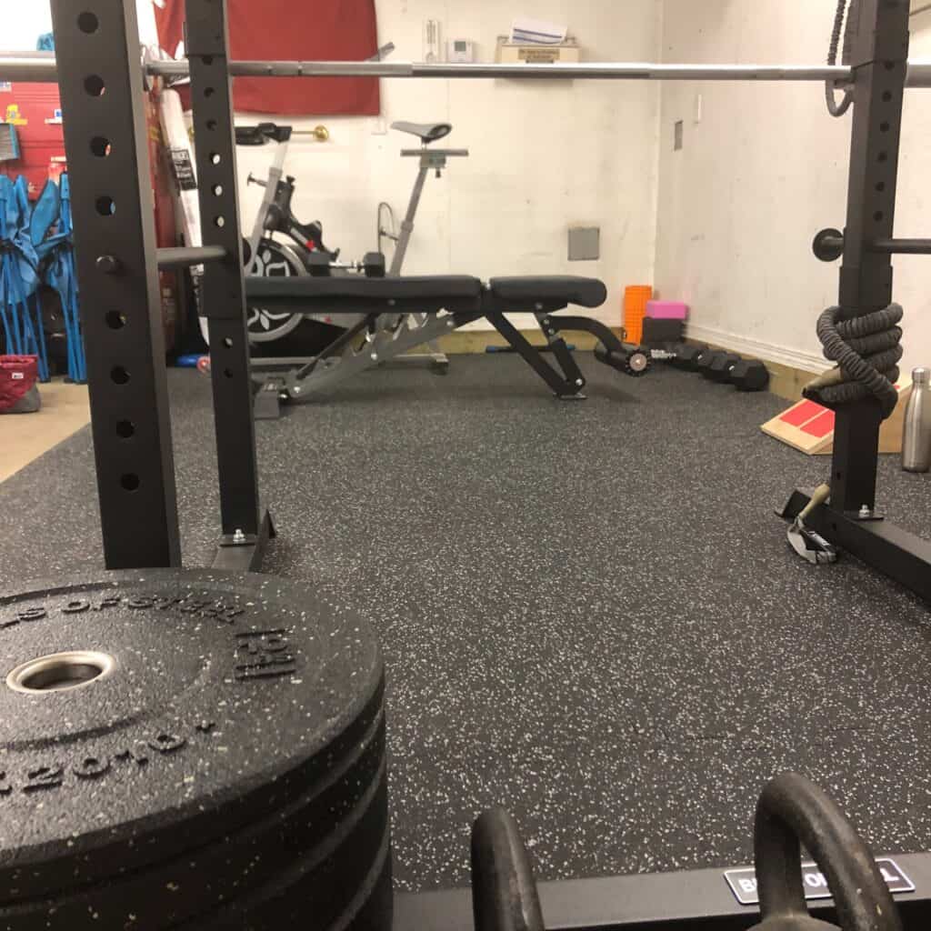 Home gym with spin bike, squat rack, dumbbells, and kettle bells