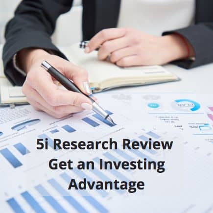 Hand holding a pen with investment charts on a table.